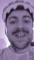a selfie of a white person, wearing either headphones or a helmet, making an odd expression. the photo is edited to be colorized into a monochrome purple-ish color palette.